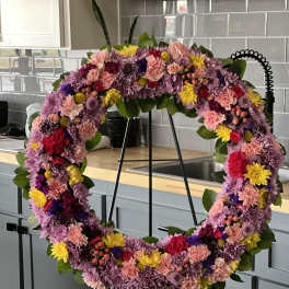 Circular floral wreath on a black stand with pink, purple, and yellow blooms
