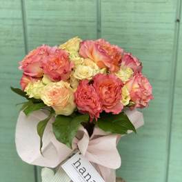 Pink and peach roses in a wrapped bouquet with a ribbon tag