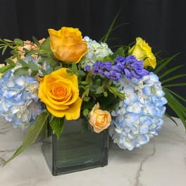 Yellow roses and blue hydrangeas in a square glass vase