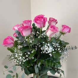 Tall arrangement of pink roses with baby's breath in a clear glass vase.