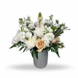 White floral arrangement in a gray vase with a peach rose