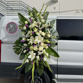 Tall white floral standing spray with purple accents on a metal easel