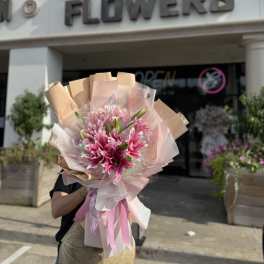 Pink lily bouquet wrapped in blush and tan paper with ribbon