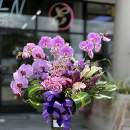 Purple orchid and rose bouquet in a glass vase with a ribbon