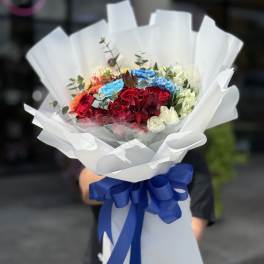 Bouquet of red, blue, white, and orange flowers wrapped in white paper with a blue ribbon