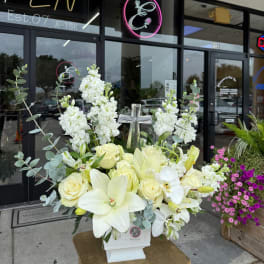White floral arrangement with roses, lilies, and a cross in a white vase