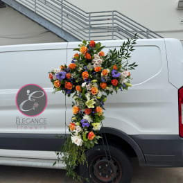 Large floral cross arrangement with orange, white, and purple flowers on a stand