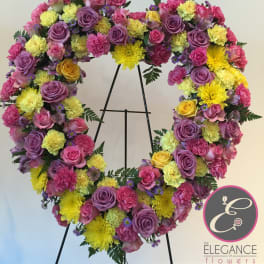 Heart-shaped floral wreath with pink, purple, and yellow blooms on a stand