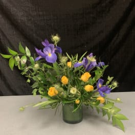 Purple iris and yellow roses arranged in a glass vase