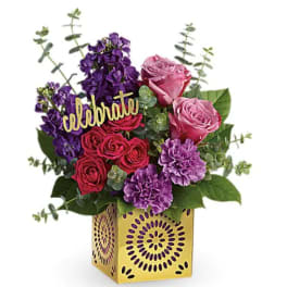 Pink and purple floral arrangement in a yellow decorative box with a "celebrate" sign