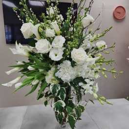 Tall arrangement of white roses, calla lilies, hydrangeas, and orchids in a clear glass vase