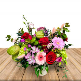 Mixed bouquet of red roses, pink daisies, and green blooms in a white vase