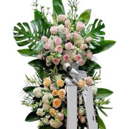 Tall standing floral spray with pink and peach roses and large tropical leaves