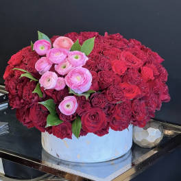 Round arrangement of red and pink flowers in a white box
