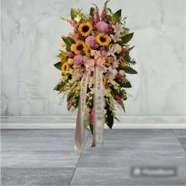 Standing floral spray with sunflowers, pink blooms, and ribbon streamers