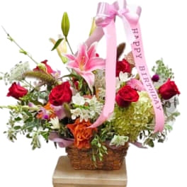 Basket arrangement with pink lilies, red roses, and a pink birthday ribbon