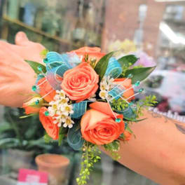 Small coral rose wrist corsage with blue ribbon and white filler flowers