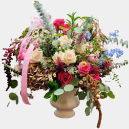 Mixed bouquet of roses and wildflowers in a beige vase with pink ribbon