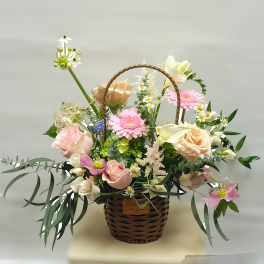 Basket arrangement of pink and peach flowers with a woven handle