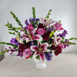 Mixed bouquet of pink roses, lilies, and purple flowers in a white vase