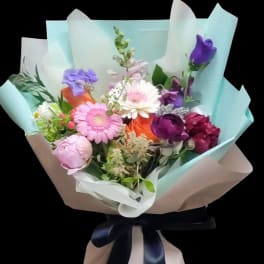 Mixed bouquet of pink, purple, white, and orange flowers wrapped in pastel paper