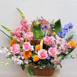 Mixed bouquet with pink roses, orange marigolds, and blue flowers in a basket