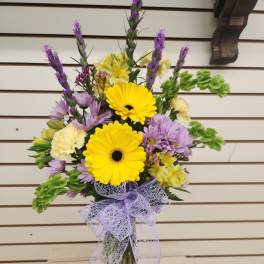 Bouquet of yellow gerbera daisies and purple flowers in a glass vase with a lavender bow