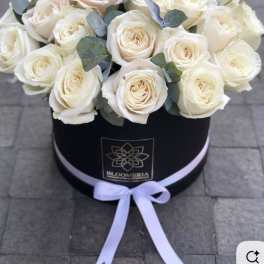 White roses arranged in a black round box with a lavender ribbon