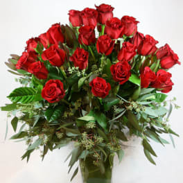 Red roses arranged in a clear glass vase with greenery