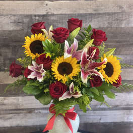 Bouquet of red roses, sunflowers, and lilies in a glass vase with a red ribbon