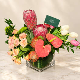 Mixed bouquet with pink protea, roses, anthurium, and white tulips in a glass vase