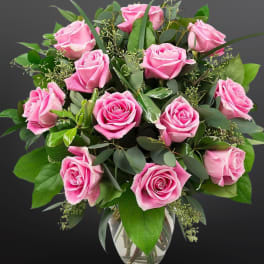 Pink roses arranged in a clear glass vase with greenery