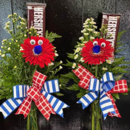 Two floral arrangements with red daisies and Hershey's bars in glass vases