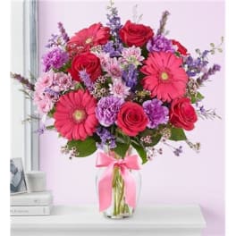 Bouquet of pink gerbera daisies and red roses in a glass vase with a pink ribbon