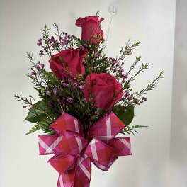 Pink roses in a clear vase with a large plaid ribbon bow