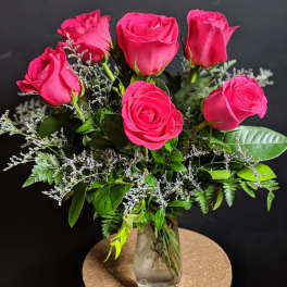 Pink roses arranged in a clear glass vase with greenery