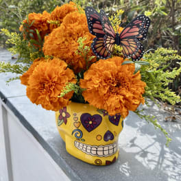 Orange marigold bouquet in a yellow skull vase with a butterfly pick