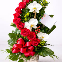 Red roses and white orchids in a square vase with a red ribbon