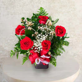 Red roses arranged in a heart-shaped design with baby's breath in a dark vase