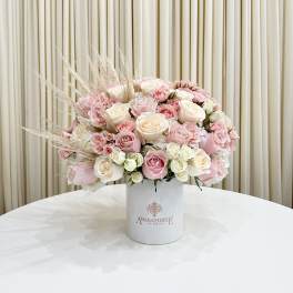 Round arrangement of blush, pink, and cream roses in a white hatbox-style container