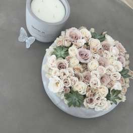 Round box of pale roses beside a white candle jar