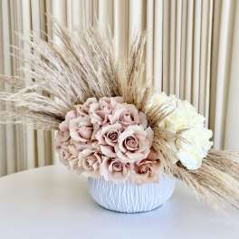 Asymmetrical arrangement of blush and ivory roses with pampas grass in a white bowl vase