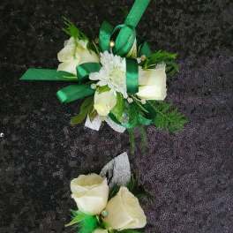 Two white rose corsages with green ribbon accents on a dark sequined background