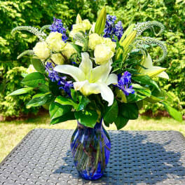 White lilies and pale roses in a blue glass vase