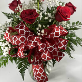 Red roses with baby's breath and a large red patterned ribbon in a glass vase