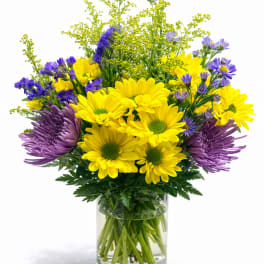 Yellow and purple flowers arranged in a clear glass vase