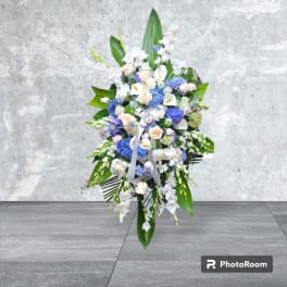 Tall standing floral spray with white and blue flowers and a white ribbon