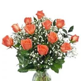 Orange roses arranged in a clear glass vase with baby's breath