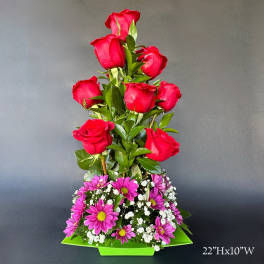 Tall arrangement of red roses and purple daisies in a green container