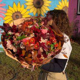 Person holding a large bouquet of mixed flowers in warm colors